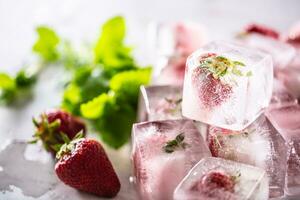 frisch Erdbeeren gefroren im Eis Blöcke mit melissa Blätter foto