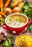Hähnchen Suppe Brühe im ein Jahrgang Schüssel mit hausgemacht Nudeln Karotte Zwiebel Sellerie Kräuter Knoblauch und frisch Gemüse foto