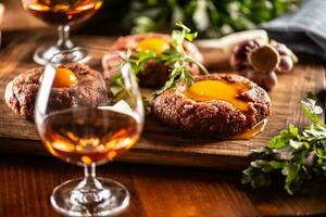 Bohnenkraut Rindfleisch Steak Tartar serviert mit Ei Eigelb, Knoblauch und Kräuter auf ein hölzern Schreibtisch. Whiskey wie ein Getränk foto