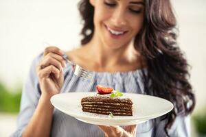 geschichtet braun adn Weiß Kuchen mit Erdbeere und Minze Blatt auf oben gehaltenen durch ein Frau mit ein Gabel foto