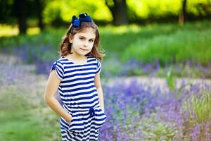 ein wenig Mädchen im ein gestreift Kleid Stehen im ein Feld von Lavendel foto