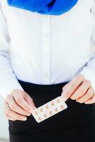 ein Frau im ein Weiß Hemd und Blau Schal halten ein Pack von Tabletten foto