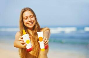 ein Frau im ein Bikini halten zwei Röhren von Sonnenschutz foto