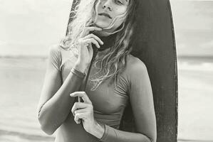 ein Frau im ein Neoprenanzug posieren mit ein Surfbrett foto
