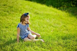 ein wenig Mädchen Sitzung auf das Gras im ein Feld foto