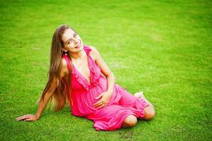 ein Frau im ein Rosa Kleid Sitzung auf das Gras foto