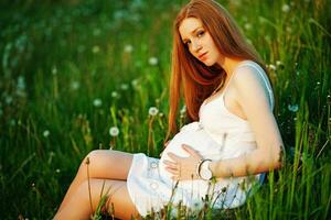 ein schwanger Frau Sitzung im ein Feld mit Löwenzahn foto