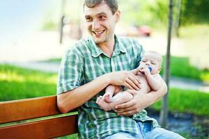 ein Mann Sitzung auf ein Bank halten ein Baby foto