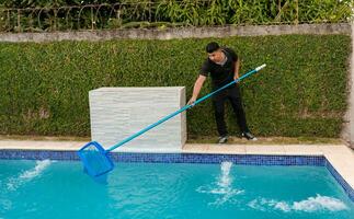 Schwimmen Schwimmbad Reinigung und Instandhaltung Konzept. Instandhaltung Person Reinigung ein Schwimmen Schwimmbad mit Abschäumer, Arbeiter Reinigung ein Schwimmen Schwimmbad mit Skimmer foto