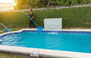 Instandhaltung Person Reinigung ein Schwimmen Schwimmbad mit Abschäumer, Arbeiter Reinigung ein Schwimmen Schwimmbad mit Skimmer. Schwimmen Schwimmbad Reinigung und Instandhaltung Konzept foto