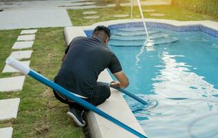 Instandhaltung Person Reinigung Schwimmen Schwimmbad mit Absaugen Schlauch. Reinigung und Instandhaltung von Schwimmen Pools mit Absaugen Schlauch. geduckt Mann Reinigung Schwimmen Schwimmbad mit Vakuum Schlauch foto