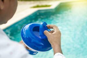 Hand von ein Schwimmbad Desinfektion Arbeiter halten ein Chlor Spender. Hände von ein Arbeiter Installation ein Schwimmbad Chlor schweben, ein Person halten ein Schwimmbad Chlor Spender foto