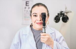 Porträt von weiblich Optiker mit Augenspiegel im das Labor. lächelnd Augenarzt halten ein Augenspiegel im das Labor foto