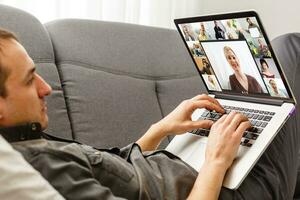 zurück Aussicht von jung Mann mit Headset und Laptop und haben Videokonferenz beim Zuhause foto