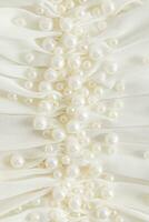 ein groß Art von Stickerei mit Perle Perlen auf ein Kleid von Beige, Elfenbein. Sanft Wellen von Seide Stoff Vorhang. Vertikale abstrakt Hintergrund. Dekor foto