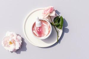 ein transparent Flasche mit ein Weiß Deckel und ein Tropfer mit ein kosmetisch Rosa Produkt, Öl, Serum Lügen im ein Linderung Weiß Schüssel unter Rose Blütenblätter. Selbstpflege. foto