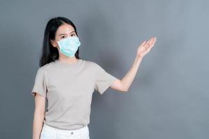 asiatische frau, die eine medizinische gesichtsmaske trägt, schützt filterstaub pm2.5 gegen verschmutzung, antismog und covid-19 mit handpräsentation