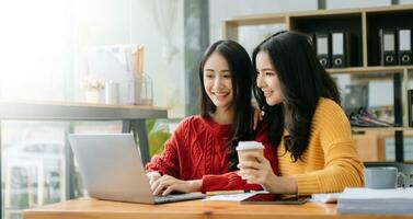 zwei attraktiv jung asiatisch weiblich Hochschule Studenten Arbeiten auf das Schule Projekt mit Laptop Computer und Tablette zusammen, genießen reden foto