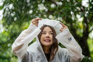 schön asiatisch Frau tragen Regenjacke und genießen im das Regen, regnerisch Jahreszeit. foto