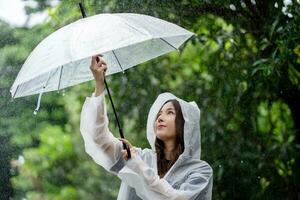 ein heiter jung Frau lächelt im ein Regenjacke im das Regen im das Mitte von Natur. foto