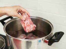 Dame Putten roh Schweinefleisch hacken im Metall Topf zum vorbereiten Suppe im Weiß sauber Zuhause Küche, Zuhause Kochen Konzept foto