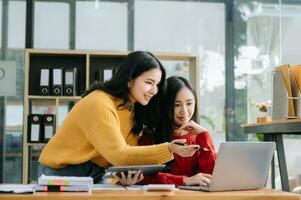 zwei attraktiv jung asiatisch weiblich Hochschule Studenten Arbeiten auf das Schule Projekt mit Laptop Computer und Tablette zusammen, genießen reden foto