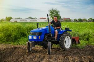 Farmer Fahrten ein Traktor über das Feld. Mahlen Boden. Arbeit im das Feld und Vorbereitung von das Land zum Pflanzen von Sämlinge oder Samen. Landwirtschaft und Agro-Industrie. Lockerung , Anbau. Pflügen foto