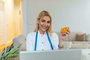 lächelnde ernährungsberaterin in ihrem büro zeigt sie gesundes gemüse und obst, gesundheits- und diätkonzept. weibliche ernährungsberaterin mit früchten, die an ihrem schreibtisch arbeitet. foto