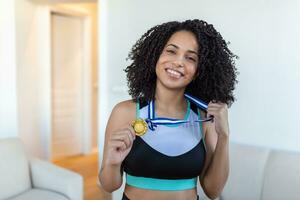 Porträt von ein attraktiv jung weiblich Athlet posieren mit ihr Gold Medaille. afrikanisch amerikanisch Athlet zeigen zuerst Platz Medaille foto