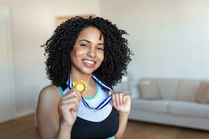 Porträt von ein attraktiv jung weiblich Athlet posieren mit ihr Gold meda. afrikanisch amerikanisch Athlet zeigen zuerst Platz Medaille foto