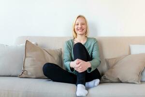 Porträt von ein lächelnd jung Frau entspannend allein auf ihr Leben Zimmer Sofa beim Zuhause im das Nachmittag foto
