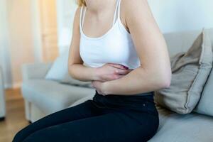 Frau, die auf dem Sofa liegt und im Wohnzimmer krank aussieht. schöne junge frau, die auf bett liegt und hände auf ihrem bauch hält. frau mit schmerzhaften bauchschmerzen im bett, menstruationsperiode foto