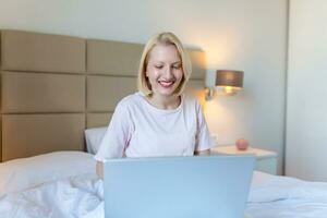 attraktive Frau im weißen Hemd mit Laptop und lächelnd am Morgen. Video-Chat und freiberufliches Arbeiten von zu Hause aus Konzept einer schönen jungen Frau mit Laptop im Bett foto