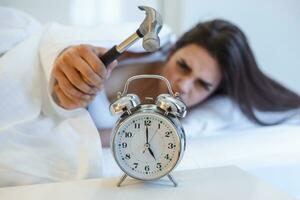 jung Frau versucht es zu brechen das Alarm Uhr mit Hammer, zerstören das Uhr. Mädchen Lügen im Bett drehen aus ein Alarm Uhr mit Hammer im das Morgen beim 5 Uhr morgens. foto