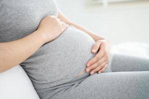 Nahaufnahme einer schwangeren Frau, die auf dem Bett sitzt und zu Hause ihren Bauch berührt. selektiver Fokus.