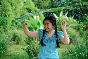 Junge Asiatin war unter einem Bananenblatt, das im grünen Gartenhintergrund Schutz vor dem Regen suchte foto