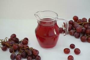 Traube Saft im ein Glas Krug mit frisch Trauben auf ein Weiß Hintergrund foto