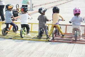 Kinder von 2-5 Jahre alt bereit zu Rennen auf Balance Fahrrad beim beginnend Punkt im ein Parkplatz Bereich, zurück Sicht, hinter Aussicht schießen. foto