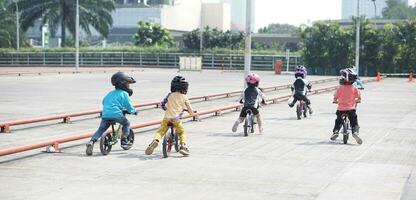 Kinder von 2-5 Jahre alt Rennen auf Balance Fahrrad im ein Parkplatz Bereich mit Zapfen wie Schiene, zurück Sicht, hinter Aussicht schießen. foto