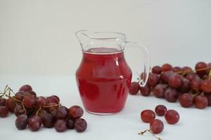 Traube Saft im ein Glas Krug mit frisch Trauben auf ein Weiß Hintergrund foto