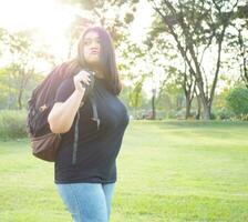 Porträt jung Frau Mädchen asiatisch mollig süß schön lange schwarz Haar einer Person tragen schwarz Hemd Stehen Rucksack bereiten zu Reise im Garten Park draussen Abend Sonnenlicht frisch glücklich entspannen Sommer- foto