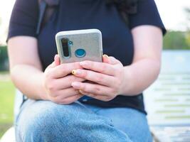 Hand jung Frau asiatisch mollig süß schön einer Person tragen schwarz Hemd aussehen Hand halten mit Clever Telefon im Garten Park draussen Abend Sonnenlicht frisch lächelnd heiter glücklich entspannen Sommer- Tag foto