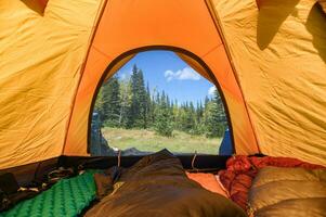 Camping mit Reisender Dehnen Beine im Schlafen Tasche auf Orange Zelt beim National Park foto