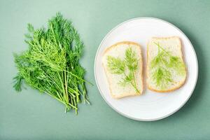 Sandwiches von Weiß Brot und frisch Dill auf ein Teller und ein Bündel von Dill auf ein Grün Hintergrund. Vitamin Kräuter im ein gesund Diät. oben Aussicht foto