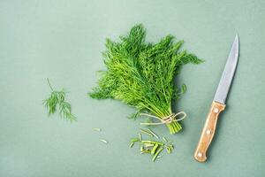ein Messer schneidet aus das Stängel von ein Bündel von frisch Dill auf ein Grün Hintergrund. Vitamin Grüns im ein gesund Diät. oben Aussicht foto