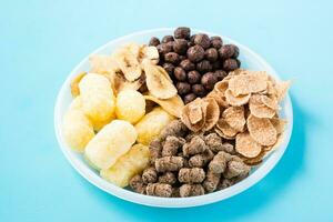 ein Teller mit anders Typen von Frühstück und Snacks Haferflocken, Getreide, Schokolade Bälle, Banane Chips und Roggen Kleie auf ein Blau Hintergrund foto