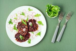 Gemüse Diät Lebensmittel. Rote Beete Steak, Rettich und Fries Salat Blätter auf ein Teller und Gabeln auf ein Grün Hintergrund foto