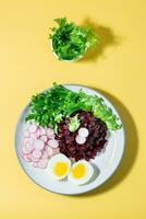 ein Diät Gericht gemacht von Gemüse. Zuckerrüben Tatar, Rettich, Fries Salat und gekocht Ei auf ein Teller auf ein Gelb Hintergrund. schwer Licht. oben und Vertikale Aussicht foto