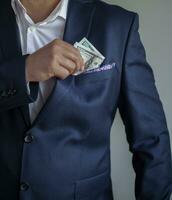 ein Mann im ein Blau passen setzt Dollar Rechnungen im seine Tasche. das Konzept von Korruption. foto