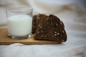 Schnitt schwarz Brot in Stücke auf ein hölzern Schneiden Tafel Nächster zu ein Glas von frisch Milch. foto